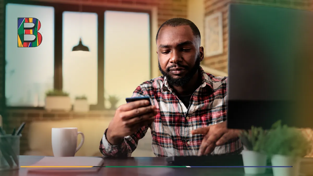 Person seated at a desk holding a bank card while using a computer.